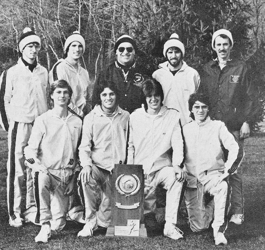 Coach Cy Fritz (dark jacket, center) and Assistant Coach Jeff Bradley (dark jacket, right) with their cross country runners after winning the NCAA DII National Cross Country Championship in 1981. FRONT ROW (kneeling, left to right): Erik Steudel, Don Williams, Greg Cauller, Bill King SECOND ROW (standing): Gary Owens, Andy Calsmer, Coach Cy Fritz, Paul Bowman, Assistant Coach Jeff Bradley