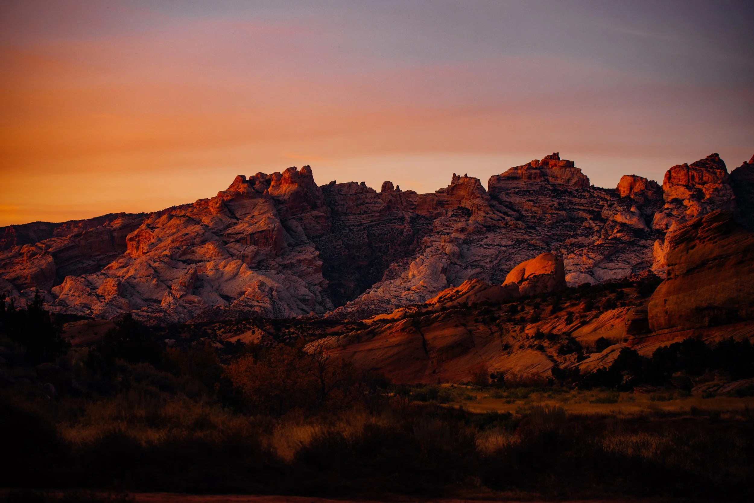 Sunset over rocky mountain landscape with warm orange and purple hues in the sky.