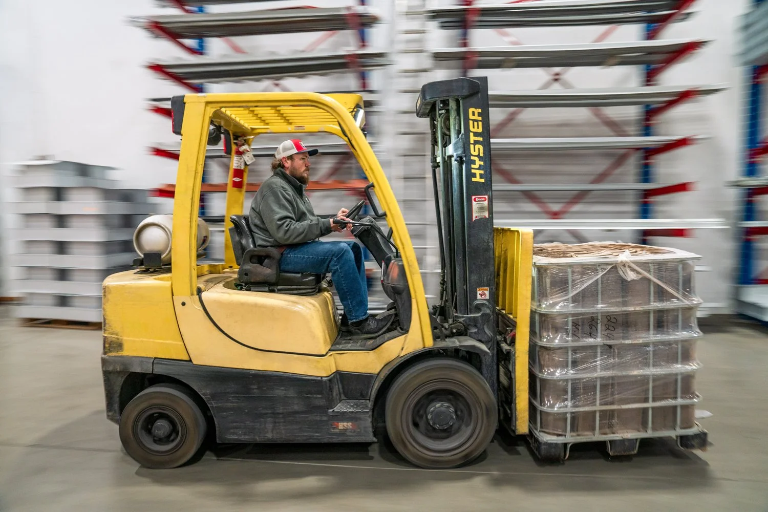 A man operating a yellow forklift in a warehouse, moving pallets stacked with boxes.