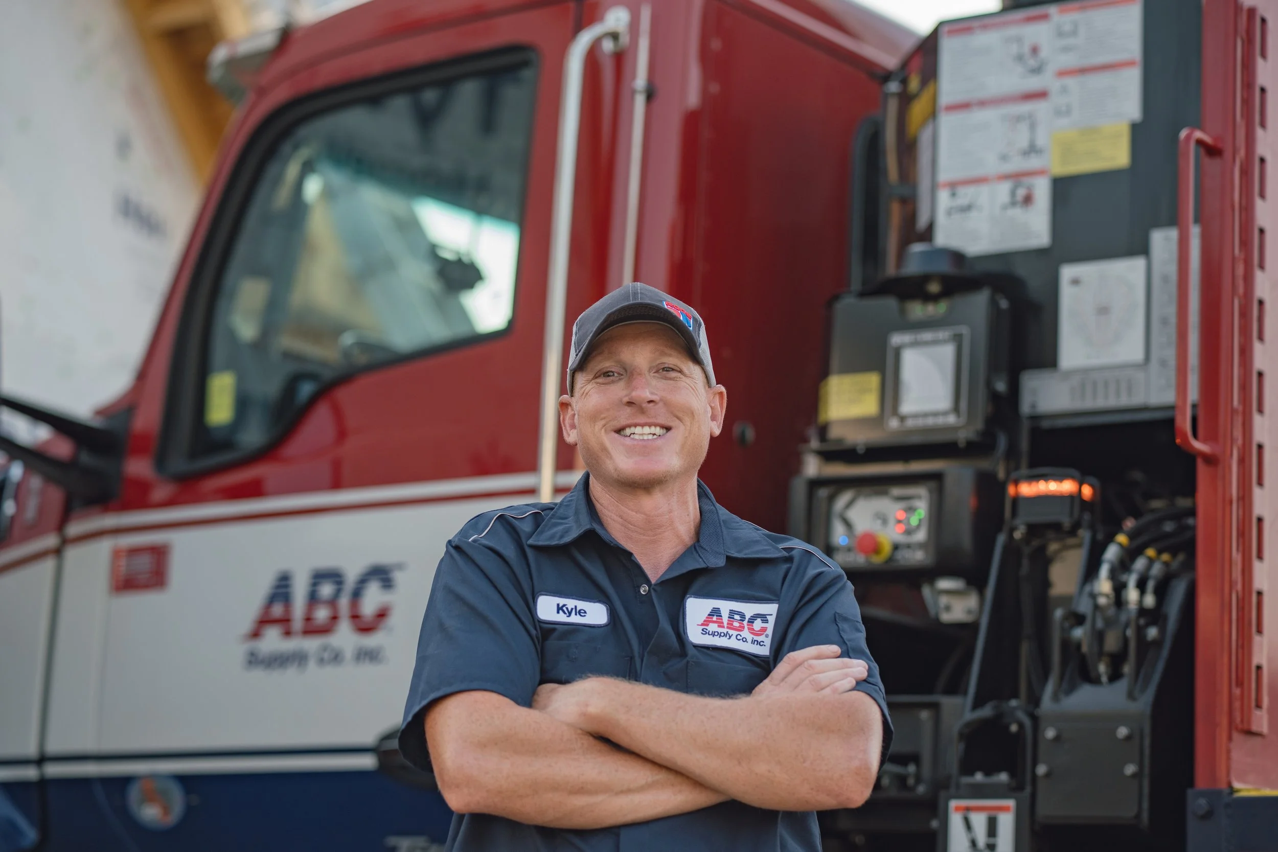 A smiling man in a uniform standing in front of a large red truck with equipment mounted on its side.