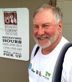"Life in the Cube" a Meat Minuteman memoir by all-star volunteer Bruce! I am a home meat monger and had been making my own sausage and bacon for a few years when the Smoking Goose opened. When they started offering classes , I started taking them. After a couple years and about five classes, I discovered that they had a program called The Minute Man. For those of you that are not familiar with it, The Minute Man program allows you to volunteer to work in production at Smoking Goose. in return, they pay you generously in meaty treats. You can do it as little or often as you like. Fortunately, I have a flexible schedule and an understanding wife, so I signed on and have been going in about one day a week. my meat skills have really improved! On my first day, I was introduced to “The Cube”. The cube is really a building within a building at the Dorman Street Meatery. My first impression was sensory overload. It is bright white and stainless steel, cold, wet, noisy, and crowded. Most of the time music is playing louder than the grinders, everything from Big Band to Heavy Metal and Rap. Inhabiting this space is a merry band of madmen who are the magicians of meat. Here they take lean and fat, salt, sugar, herbs and spices and turn it into all those great products. After spending some time in there, several things have struck me. The first and foremost is that everything is handcrafted from the highest quality ingredients. Sure, machines grind and mix sausage meat, but the final assembly is all by hand. I have learned to stuff, tie and truss hams, sausages of all types and shapes, duck breasts, you name it. Everyone in The Cube can perform multiple roles, often shifting from one task to another and back again as the ebb and flow of production goes on. Everyone also has a careful eye for quality. If something slips by one person, someone else will catch and correct it. The second thing is the quantity of product that is produced, especially given the handcrafted nature of it. Ever wonder what a half-ton of bacon looks like? Sign up for Minute Man duty and you’ll get your chance. The Goose ships all over the country so it is a constant balancing act to have product ready to go given that much of it has a six week or longer aging period. One batch comes out, the next goes in. The last big thing I noticed is the amount of creativity. There is a constant search for new and different recipes for sausage and meats. A number of people contribute and often someone will bring in a test batch for everyone to try. Critiques are made and formulas adjusted to get the final product just right. The same applies to production techniques. There is always a search to find better ways to keep quality high and achieve the production needed. It has certainly been a refreshing and enjoyable time. I can’t recommend it enough for anyone interested in improving their home sausage making skills or just wanting to learn the basics to get started. All the guys in the cube are pretty patient and willing to share their knowledge. I am a hunter and have always butchered my own meat, but my knife skills are also vastly improved. (And I still have all ten digits at full length!) If you are interested in giving the Meat Minuteman (and Woman) Program a try, i encourage you to sign up. Oh, and that understanding wife, she now places her orders for the products I am working for!