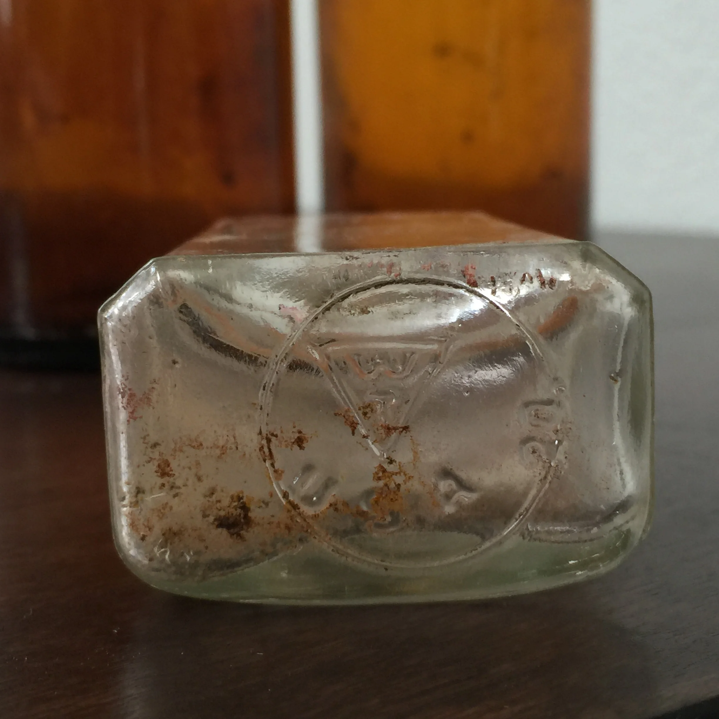 The base of the smaller, clear glass bottle with imprints indicating when and where it was manufactured.