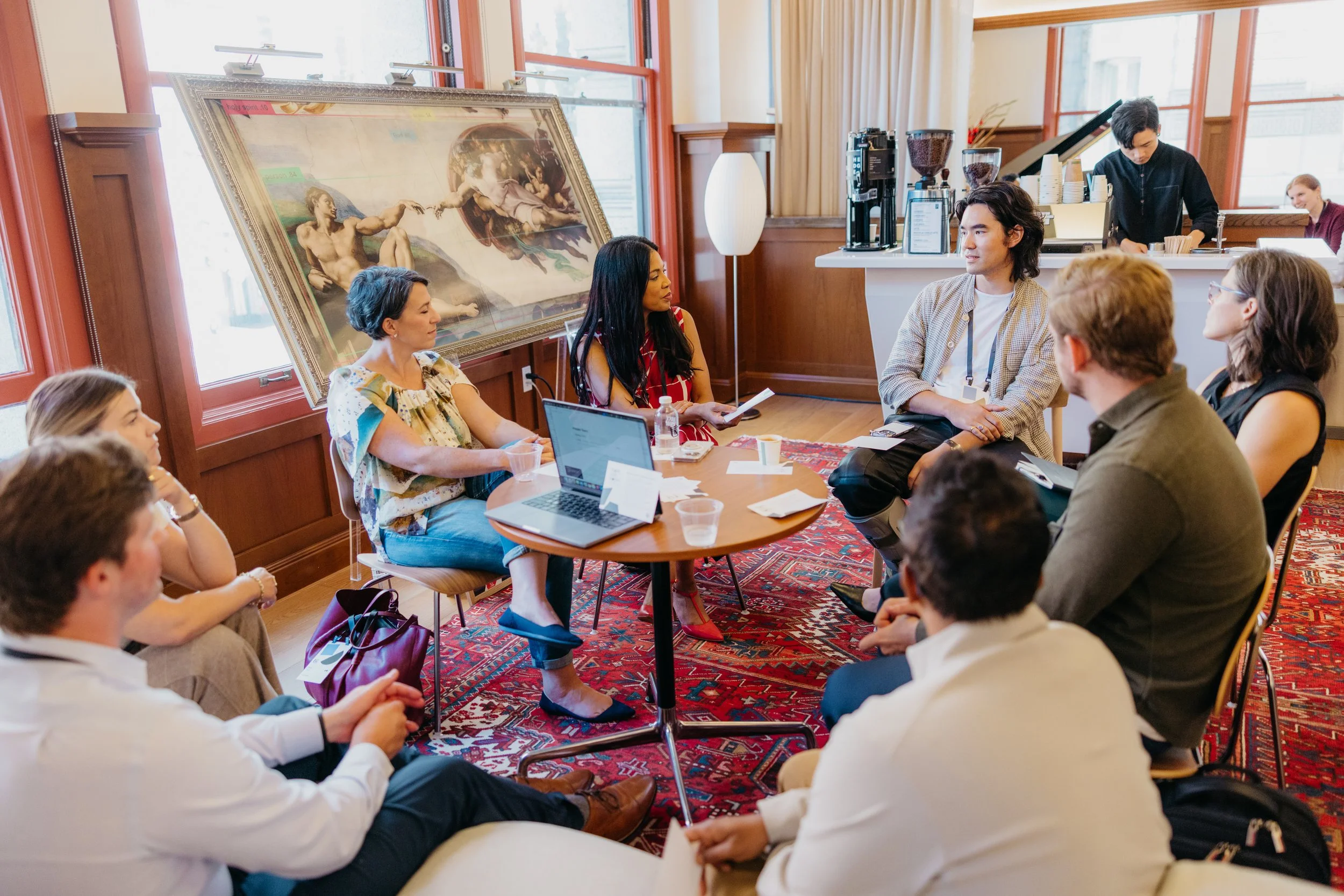 A group of people sitting in a circle in a room with wooden paneling and a large painting of Michelangelo's Creation of Adam on the wall. Make With Notion Executive Summit in San Francisco