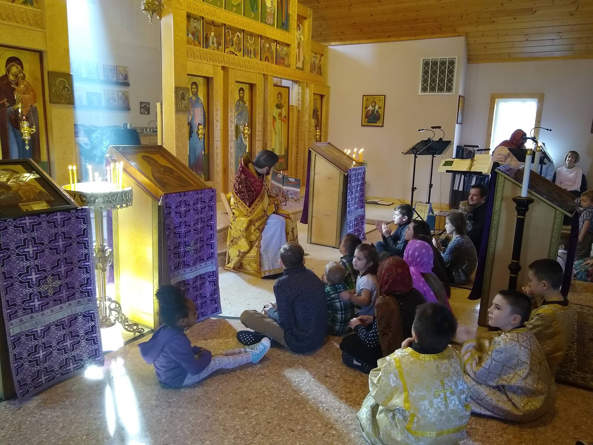  children sitting in front of priest while he reads book 