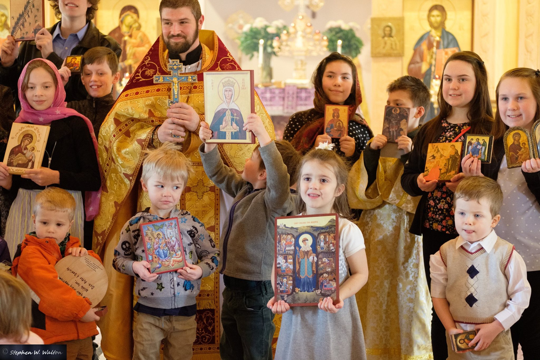  closeup of children holding icons standing with priest 