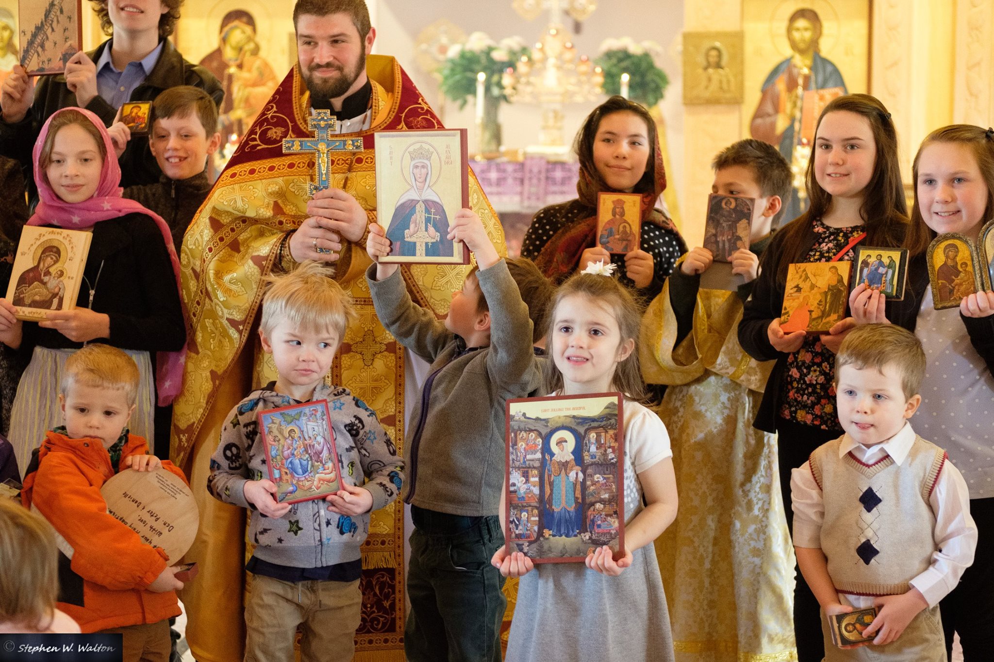 closeup of children holding icons standing with priest