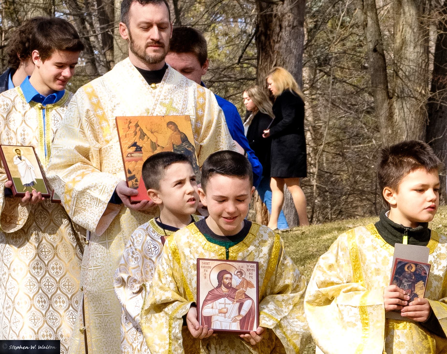  older altar servers behind young altar servers in procession outside holding icons 