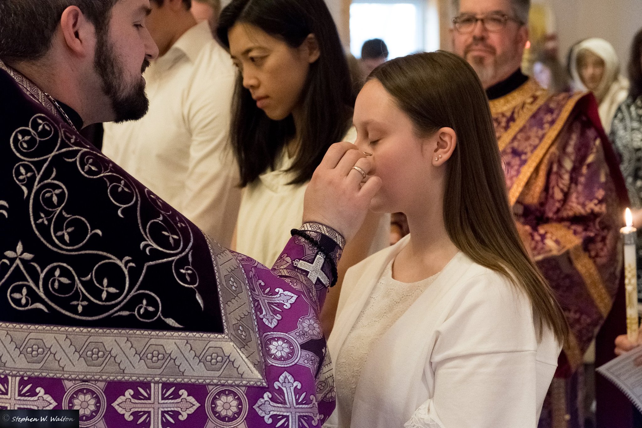 priest anointing young woman for chrismation with deacon behind her 