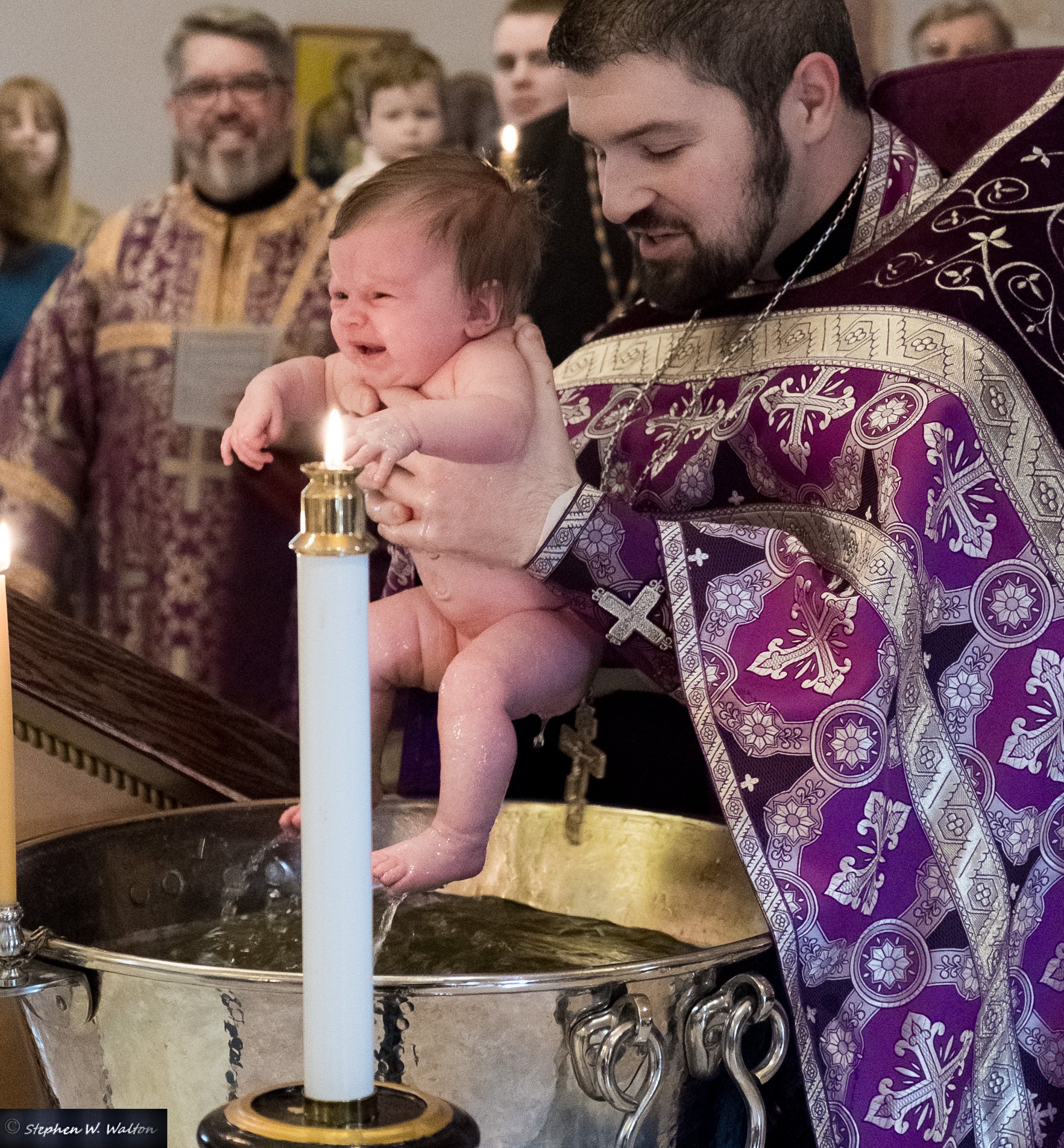  priest lifting infant out of baptismal font  