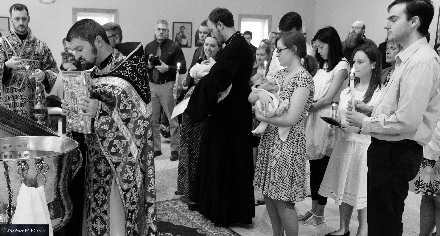  priest leading newly received in procession around the baptismal font black and white 