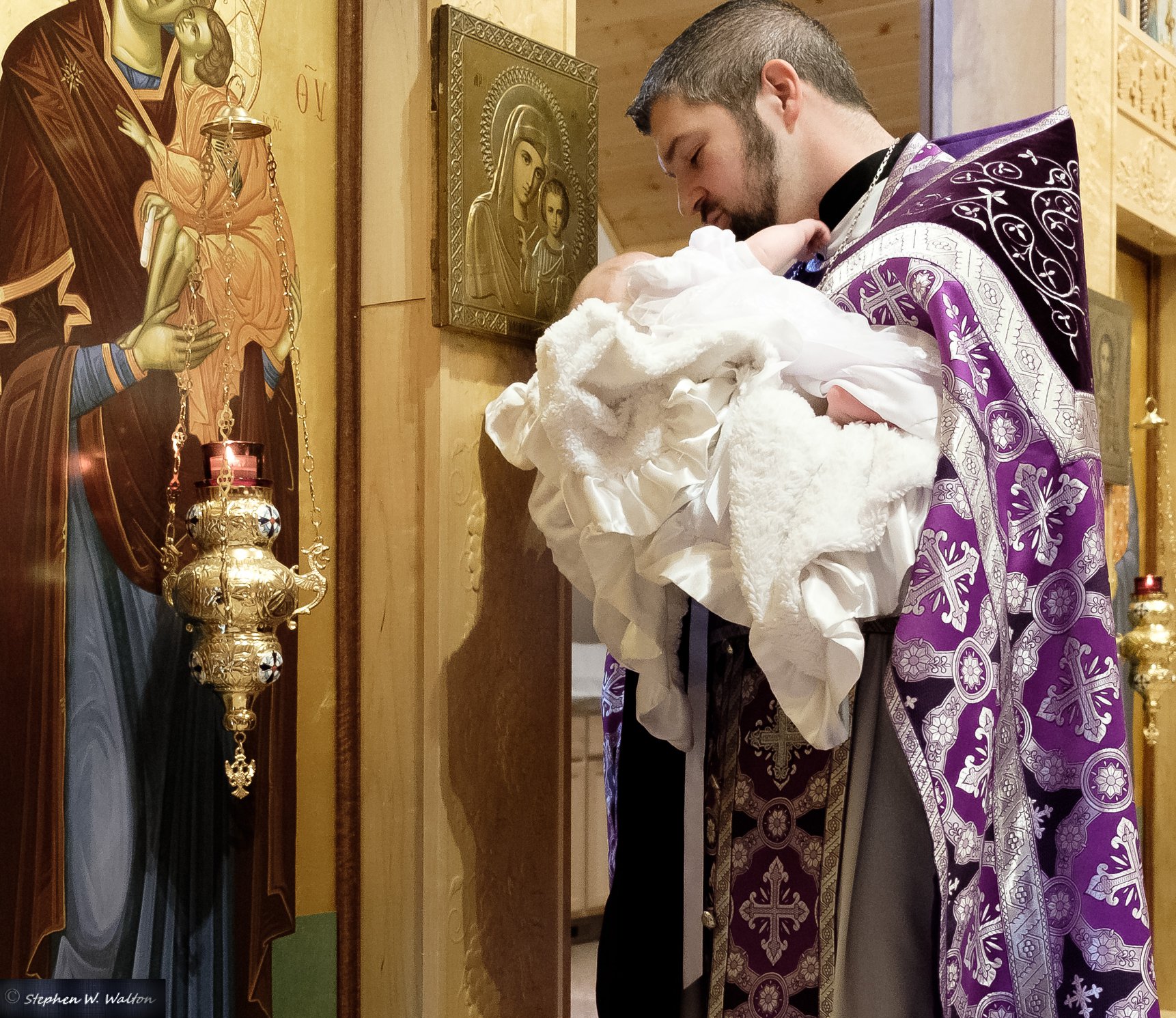  priest carrying infant up to icons 