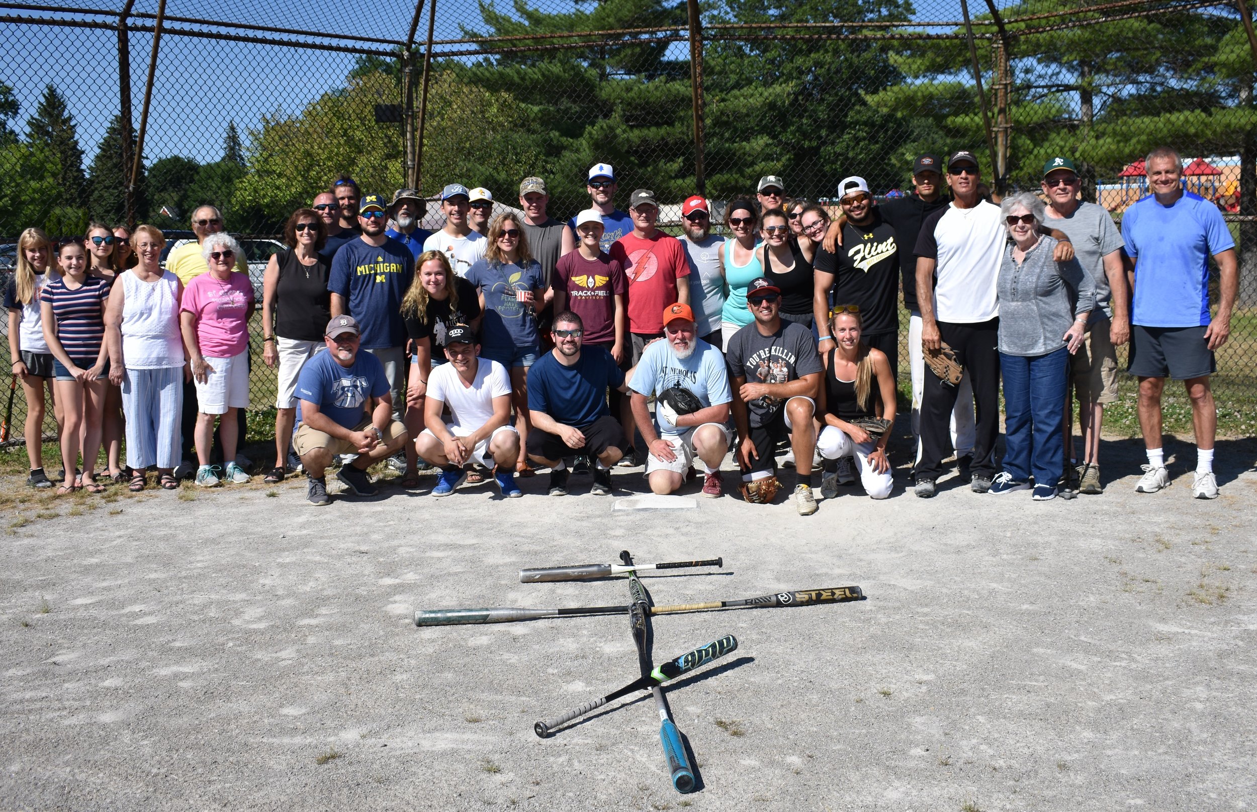  Participants of pan orthodox softball game behind home plate with bats in shape of cross in foreground 