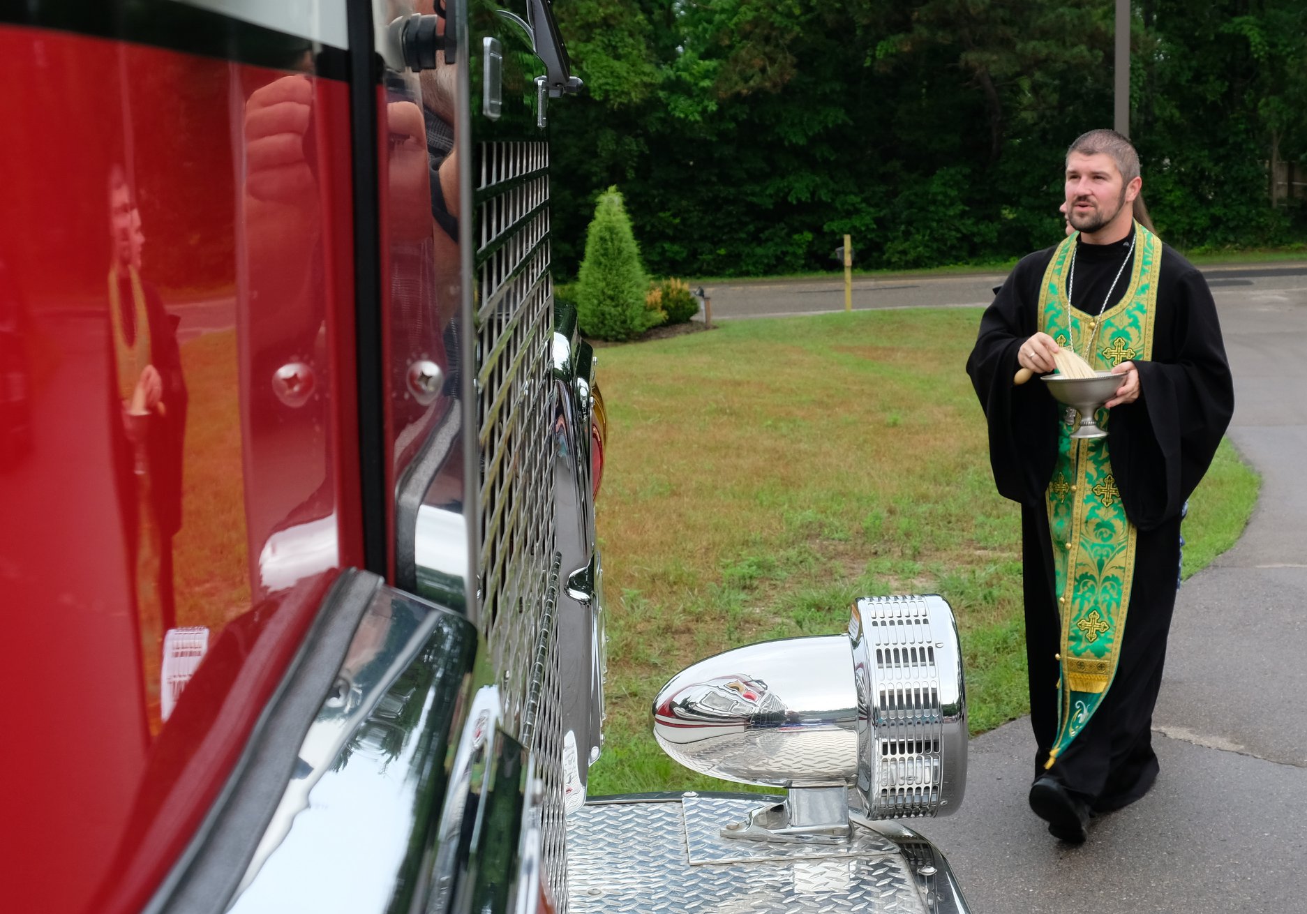  priest walking to fire truck to bless with holy water 