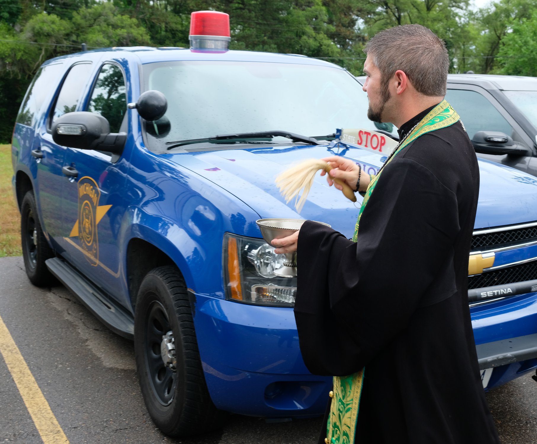 priest blessing state trooper SUV with holy water 