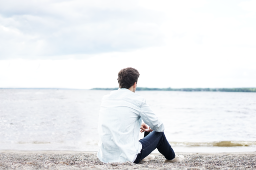 man sitting on beach looking out into the water