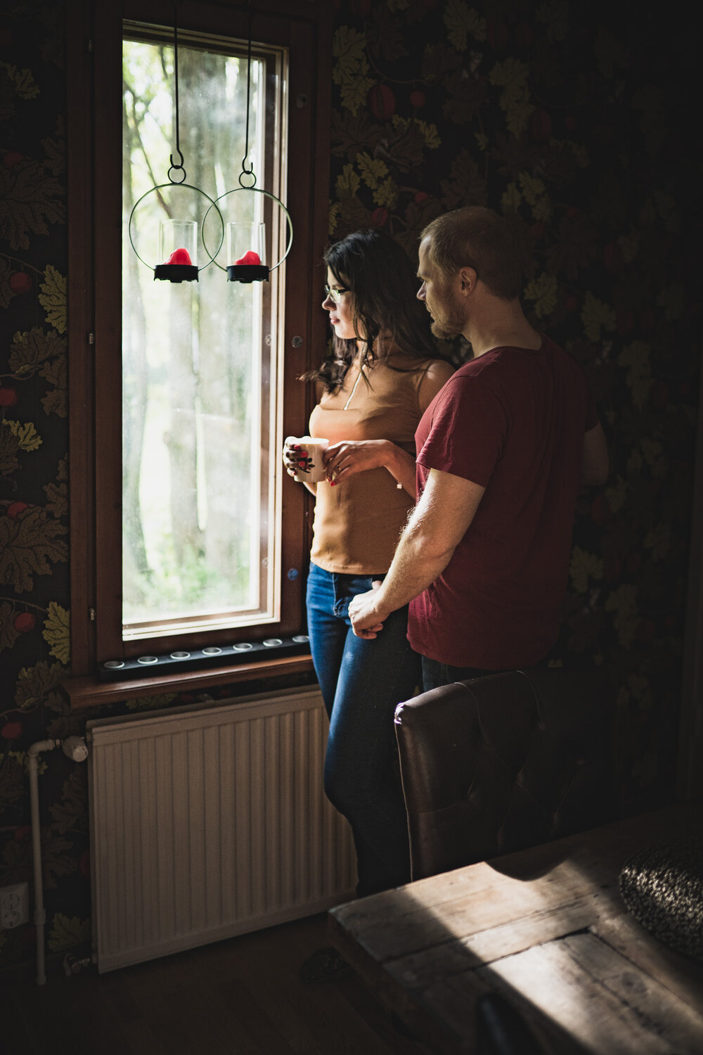 Beautiful couple standing at the window during an in-home photo session in Kuopio, Finland