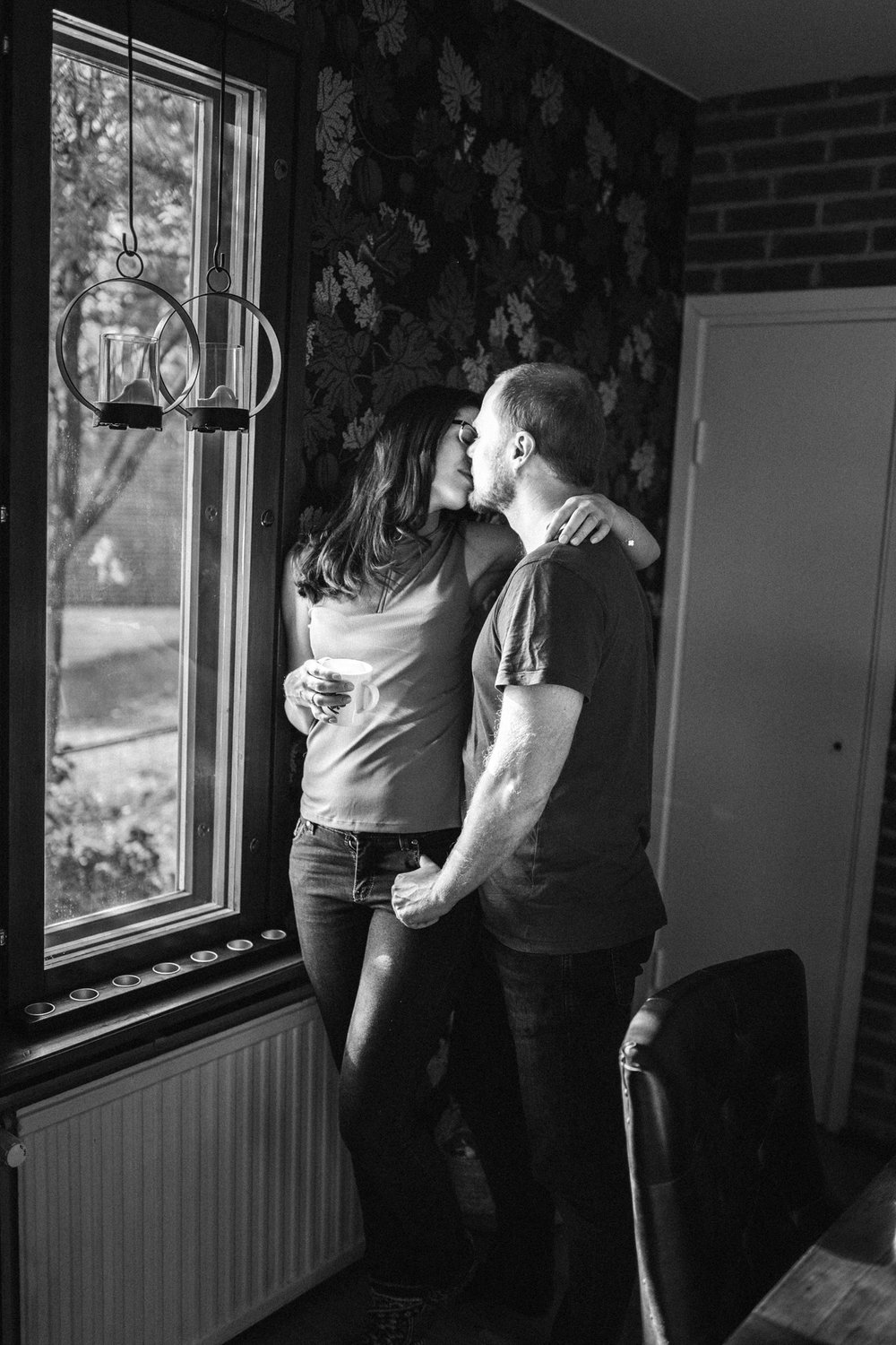 Beautiful couple standing at the window during an in-home photo session in Kuopio, Finland