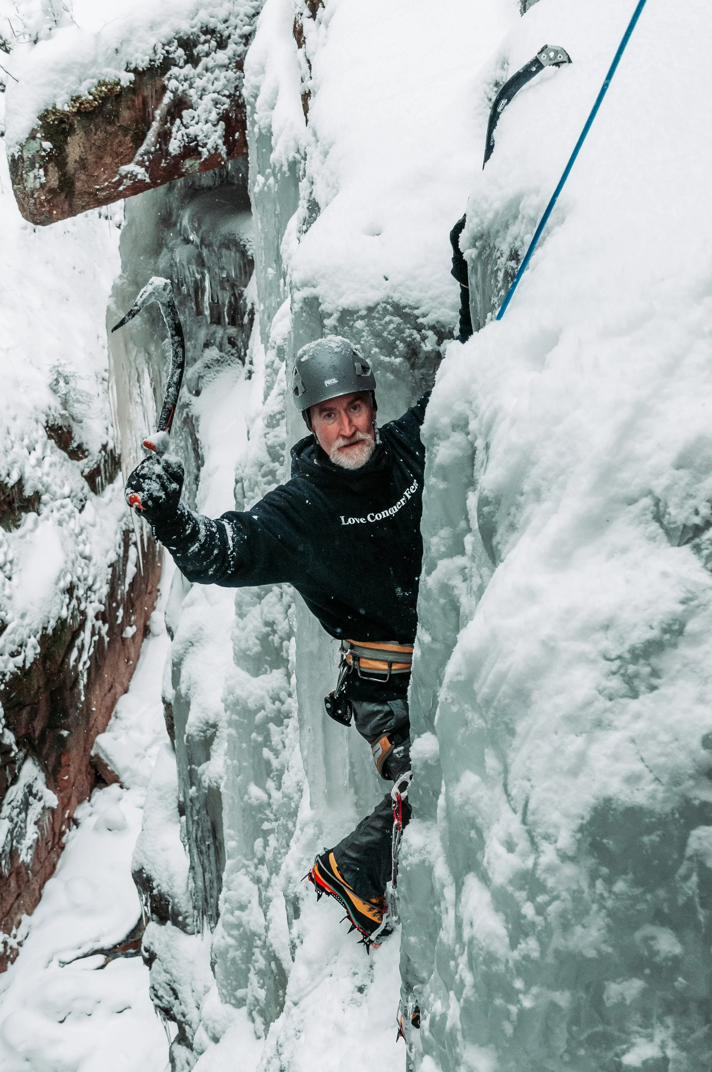 Ice climber smiling while climbing with ice tools