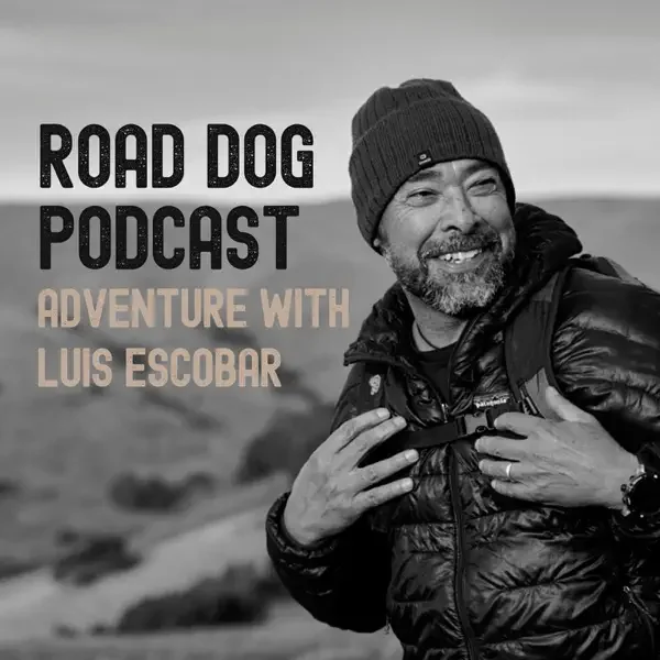 Black and white photo of Luis Escobar smiling outdoors with a backpack, wearing a beanie and jacket, for the Road Dog Podcast titled "Adventure with Luis Escobar."