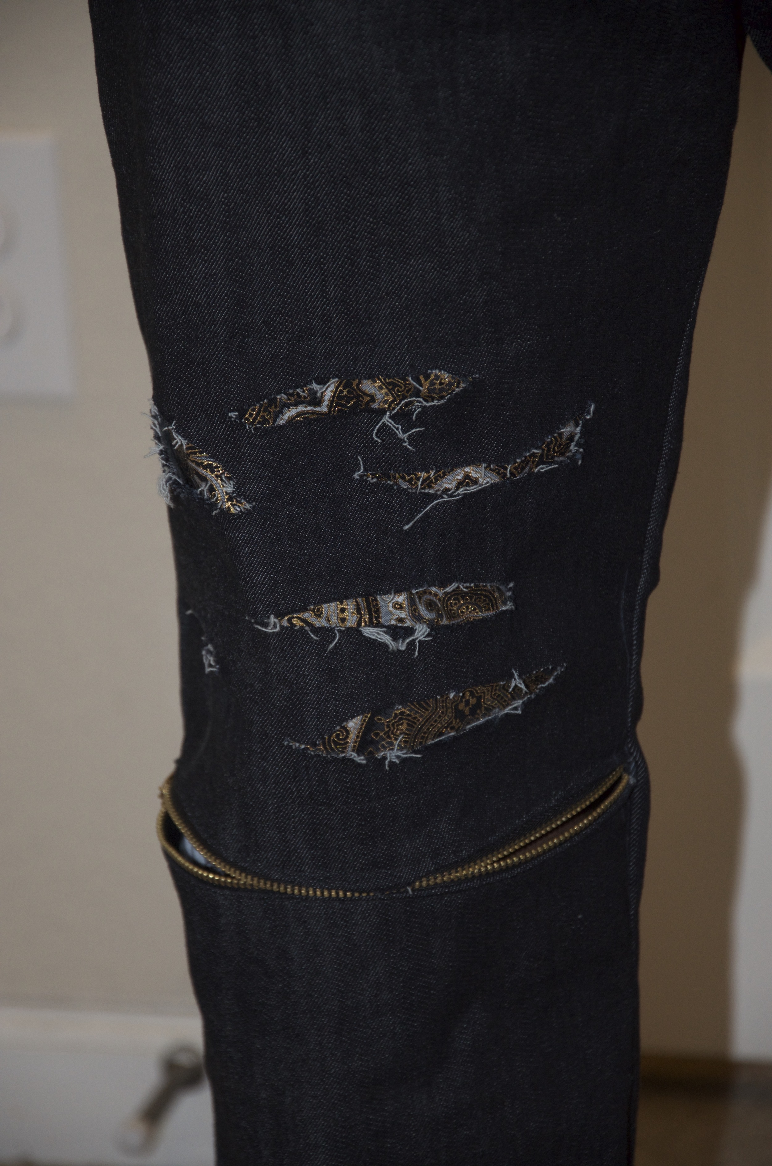 View of Right Knee with zipper installation at the knee. Light distressed cuts at lower thigh with fabric attachment at lower thigh.