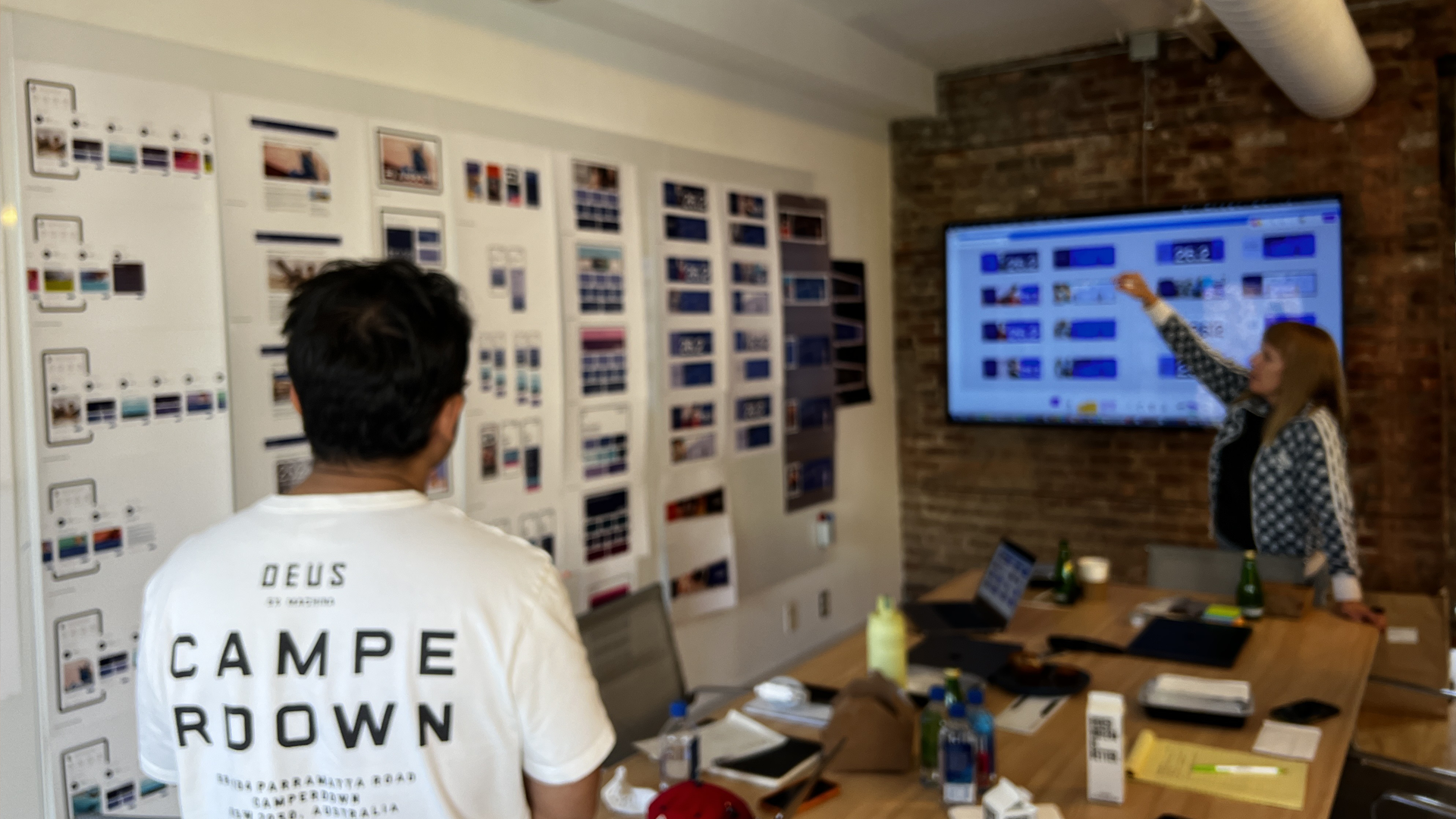 People having a design meeting with printed visuals on walls and a slideshow on a screen.