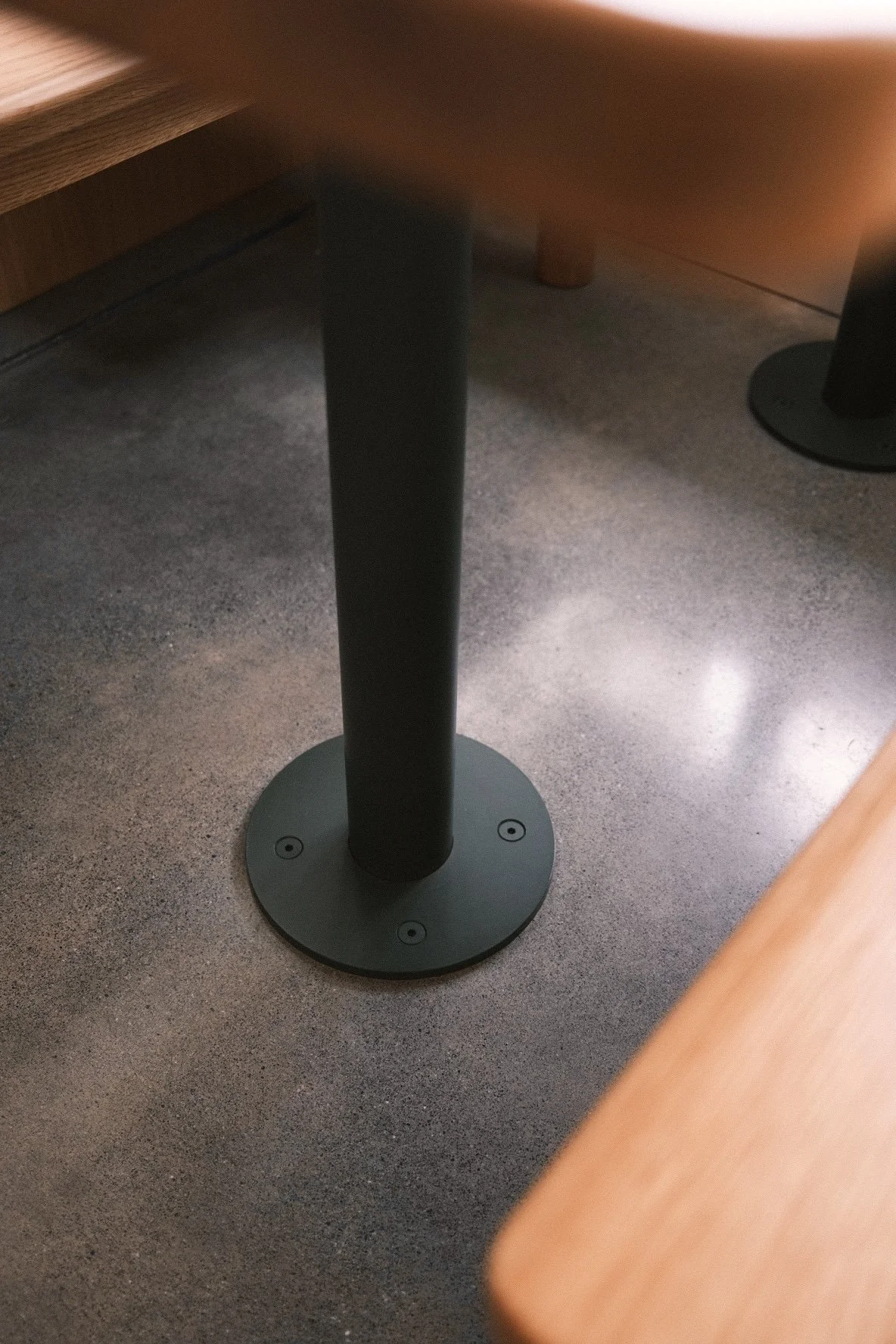 Blackened steel table base plate bolted to a polished concrete floor, restaurant furniture detail