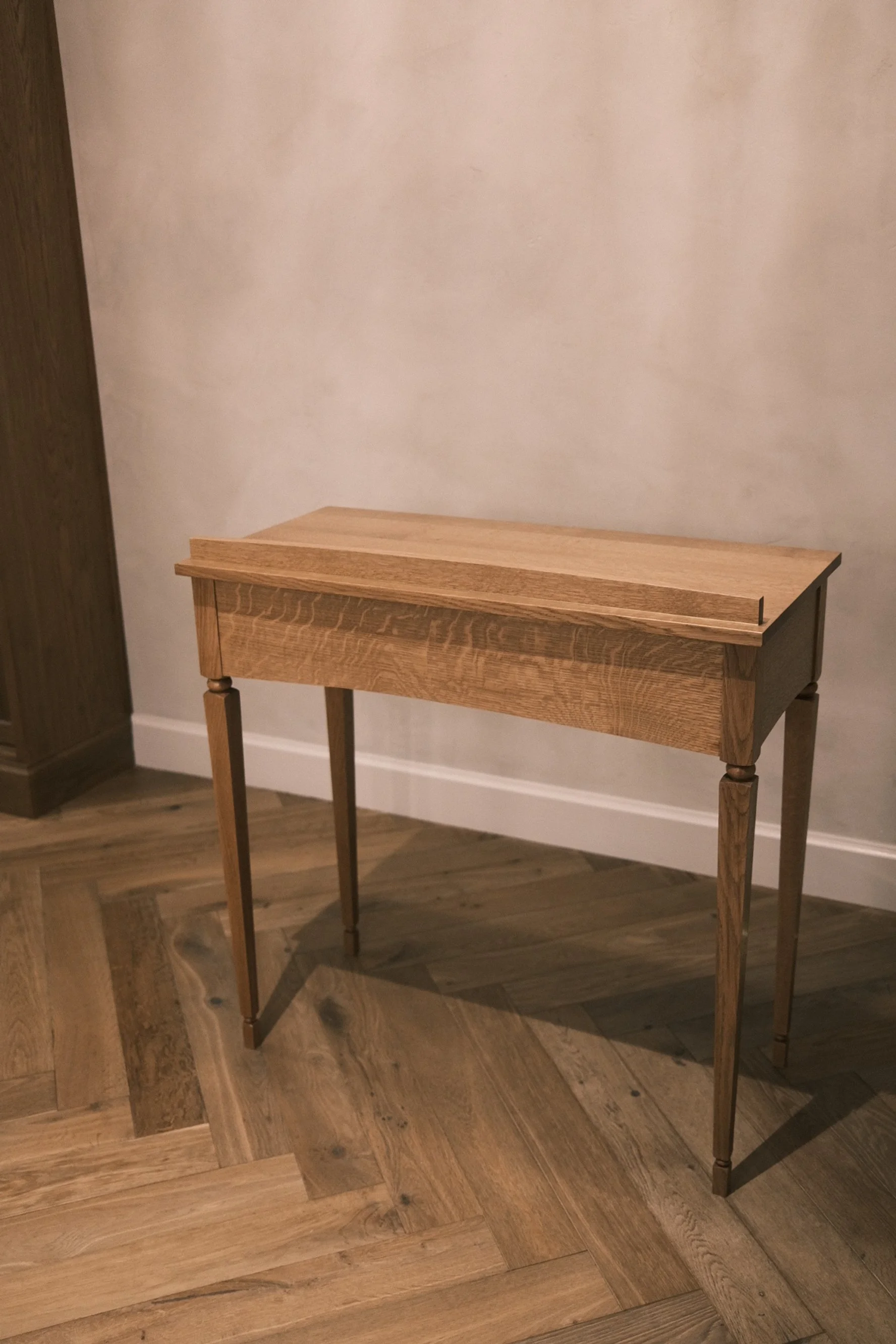 White oak console table with tapered legs and molded top on a herringbone floor