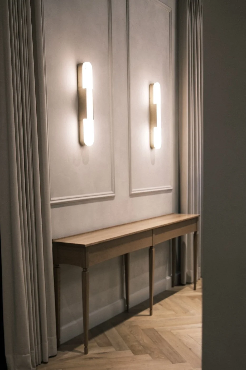 Slim white oak console with tapered legs below plaster sconces and wall paneling at The Kitchen, Sacramento