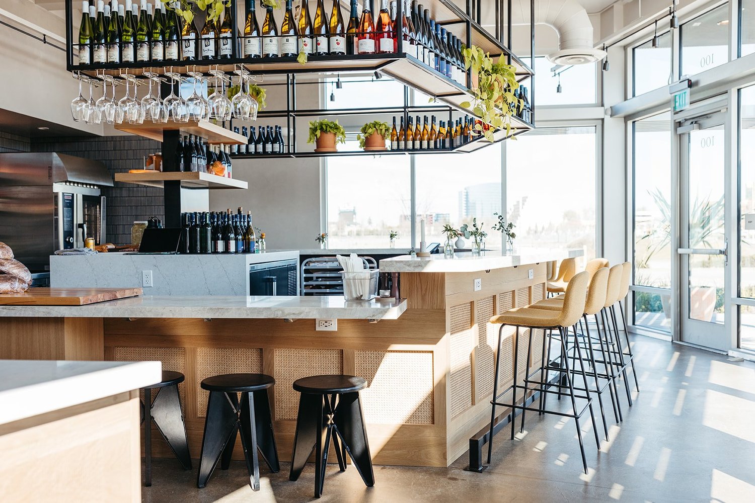 Café bar with textured white oak counter front and suspended steel bottle rack at Franquette
