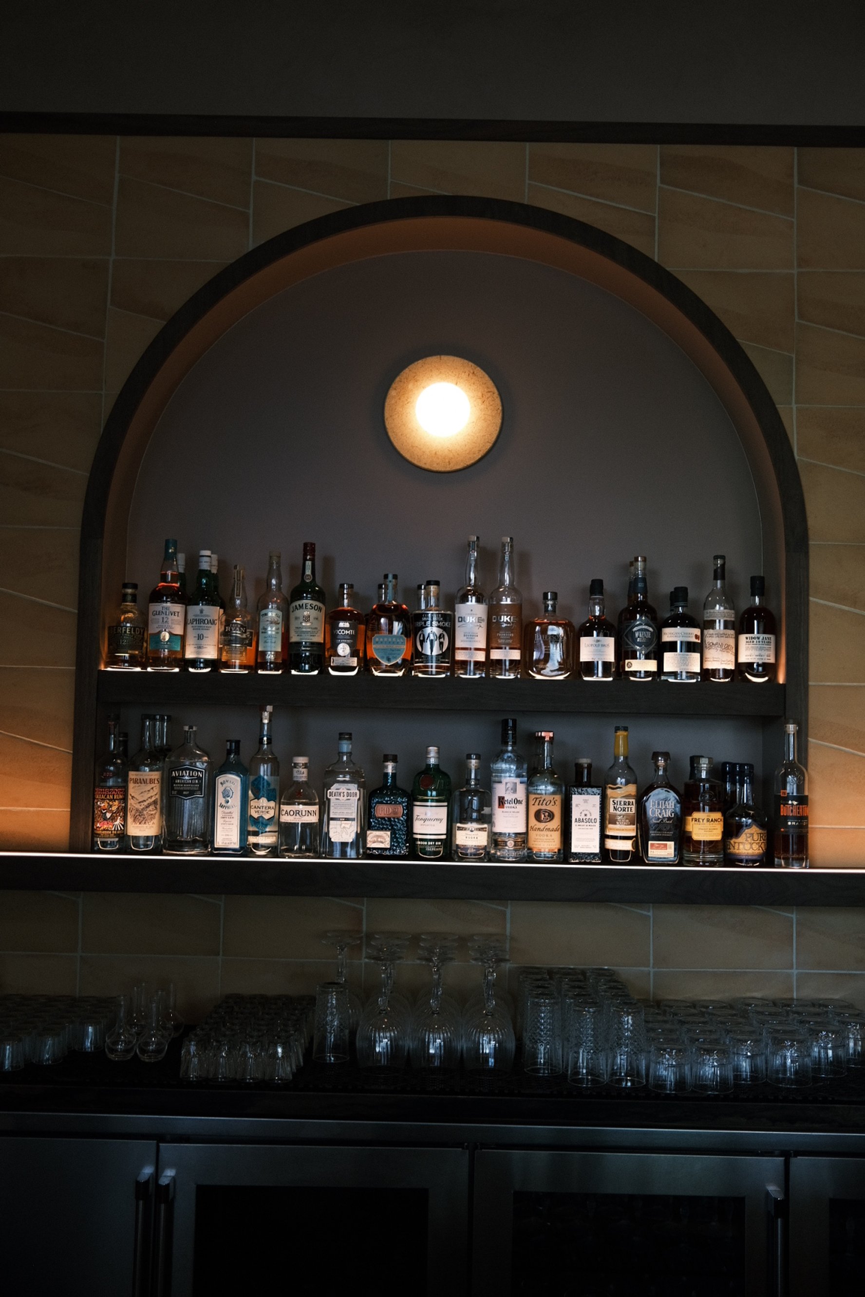 Arched back-bar niche with floating spirits shelves and globe sconce at Cantina Pedrigal
