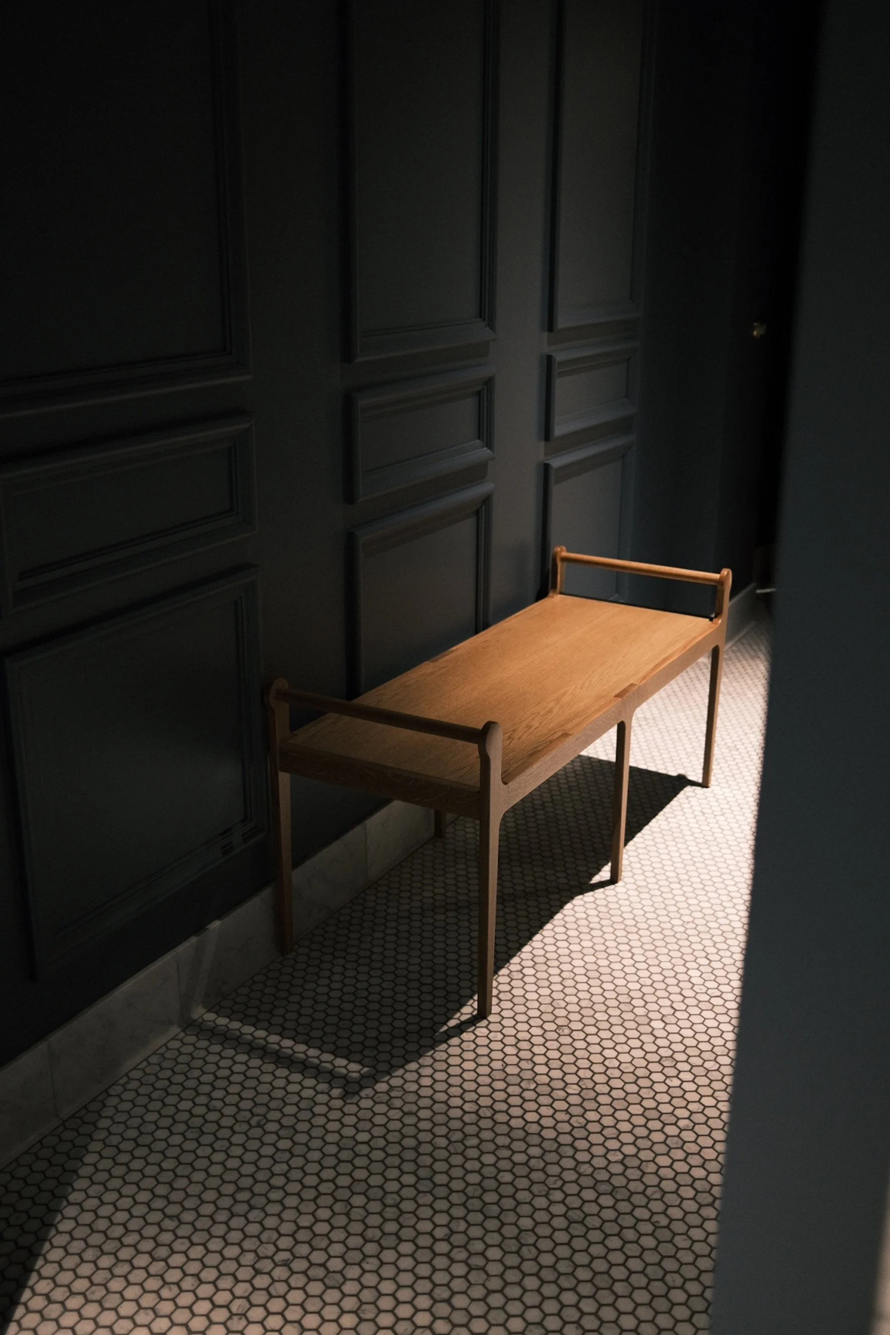 White oak open-arm bench on mosaic tile against dark paneling at The Kitchen, Sacramento