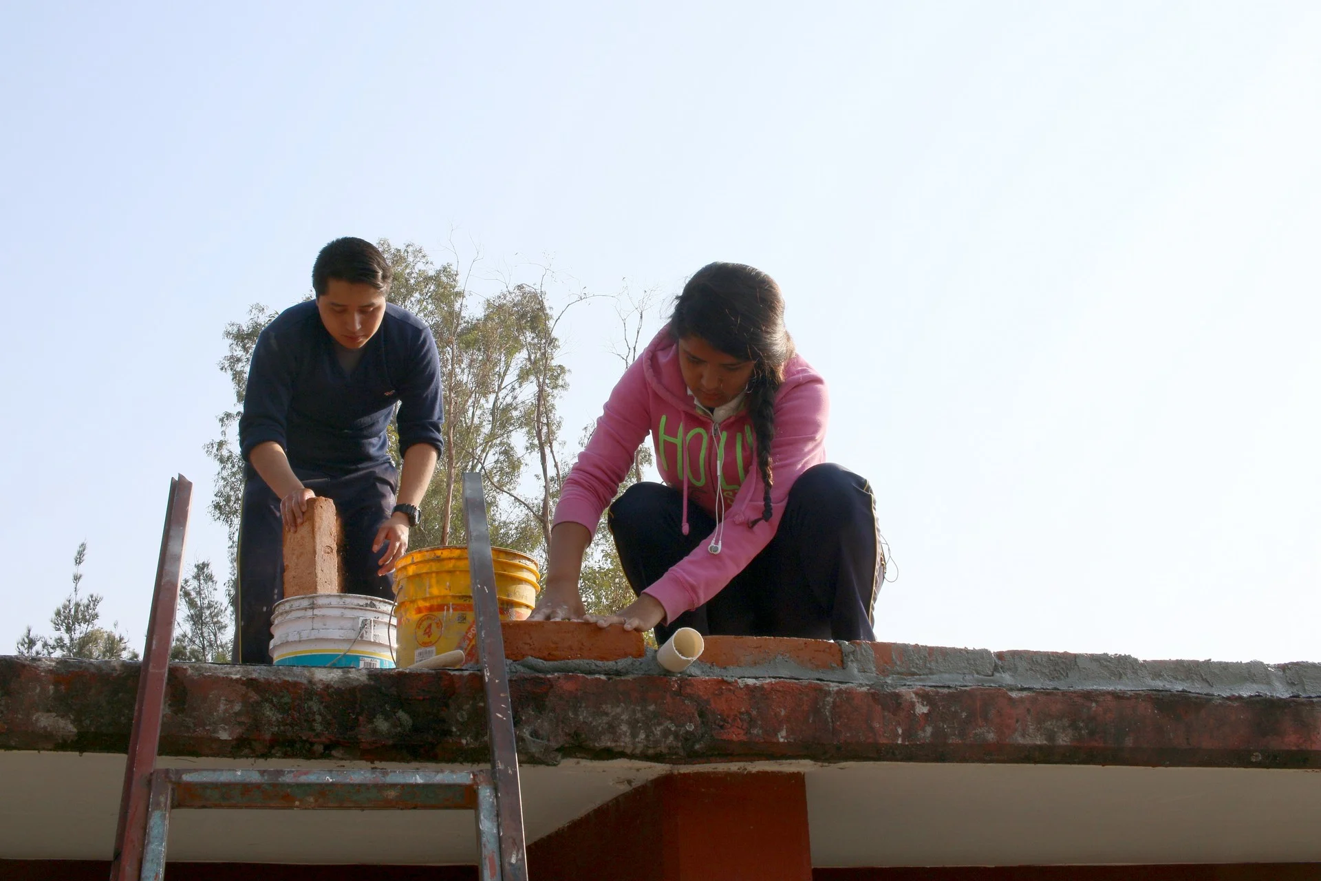 Dos estudiantes ponen ladrillos en el techo que formarán la canalización a las tuberías.
