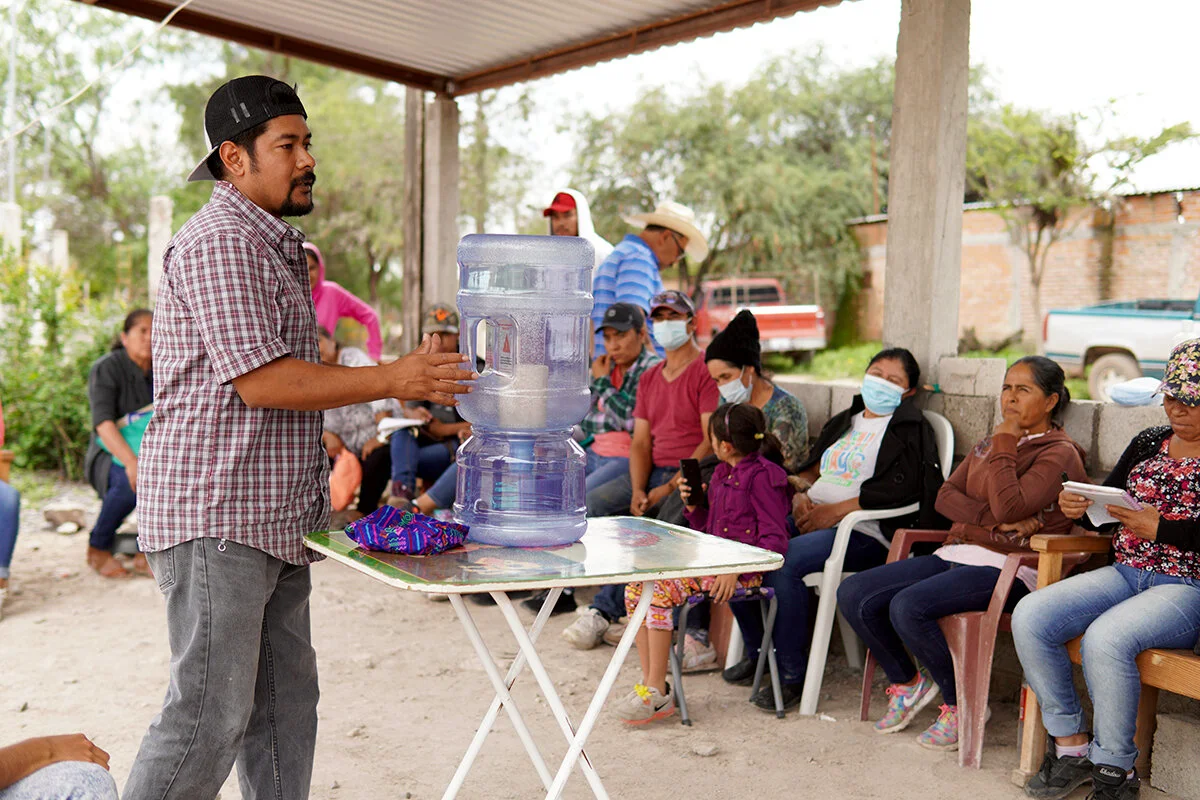 Foto: Saúl, Coordinador de Proyectos Comunitarios de Caminos, le explica a un grupo de miembros comunitarios la forma correcta de usar el sistema de filtrado Aguadapt.