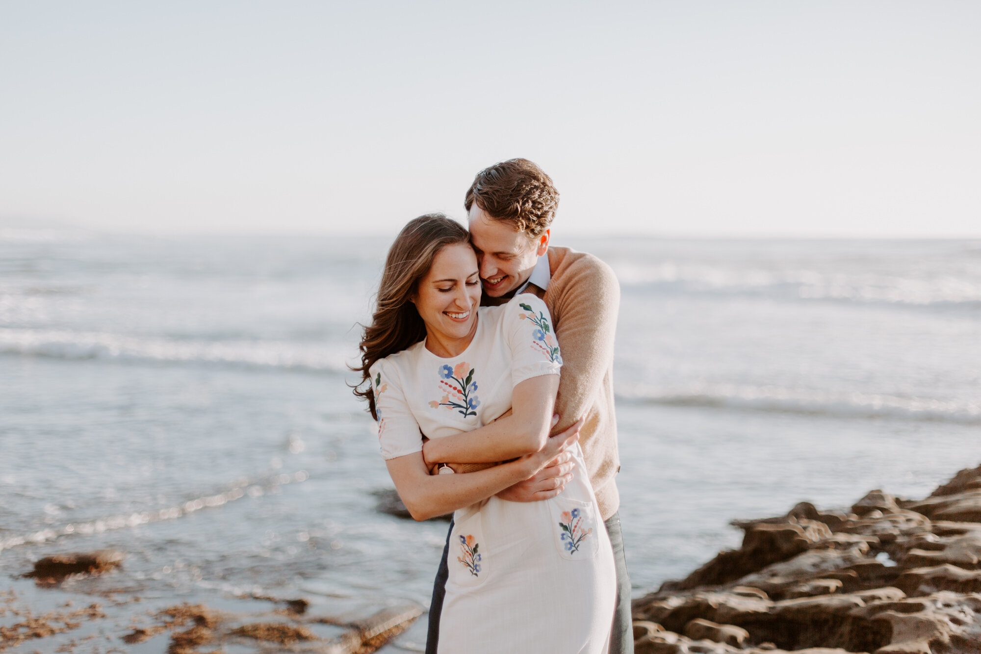 La Jolla Engagement Photos in San Diego with beach cliff and tide pools and on the sand.  Wore a white floral dress and took their engagement photos for their wedding by Kara Reynolds photography