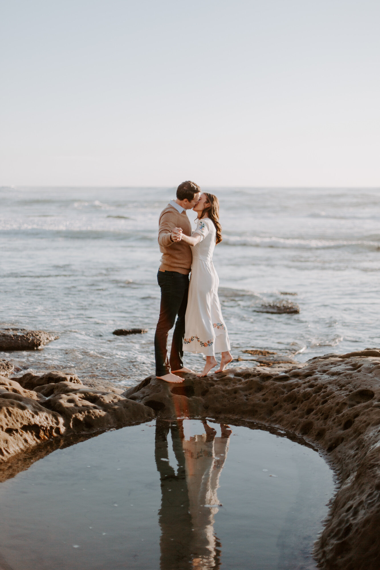 La Jolla Engagement Photos in San Diego with beach cliff and tide pools and on the sand.  Wore a white floral dress and took their engagement photos for their wedding by Kara Reynolds photography