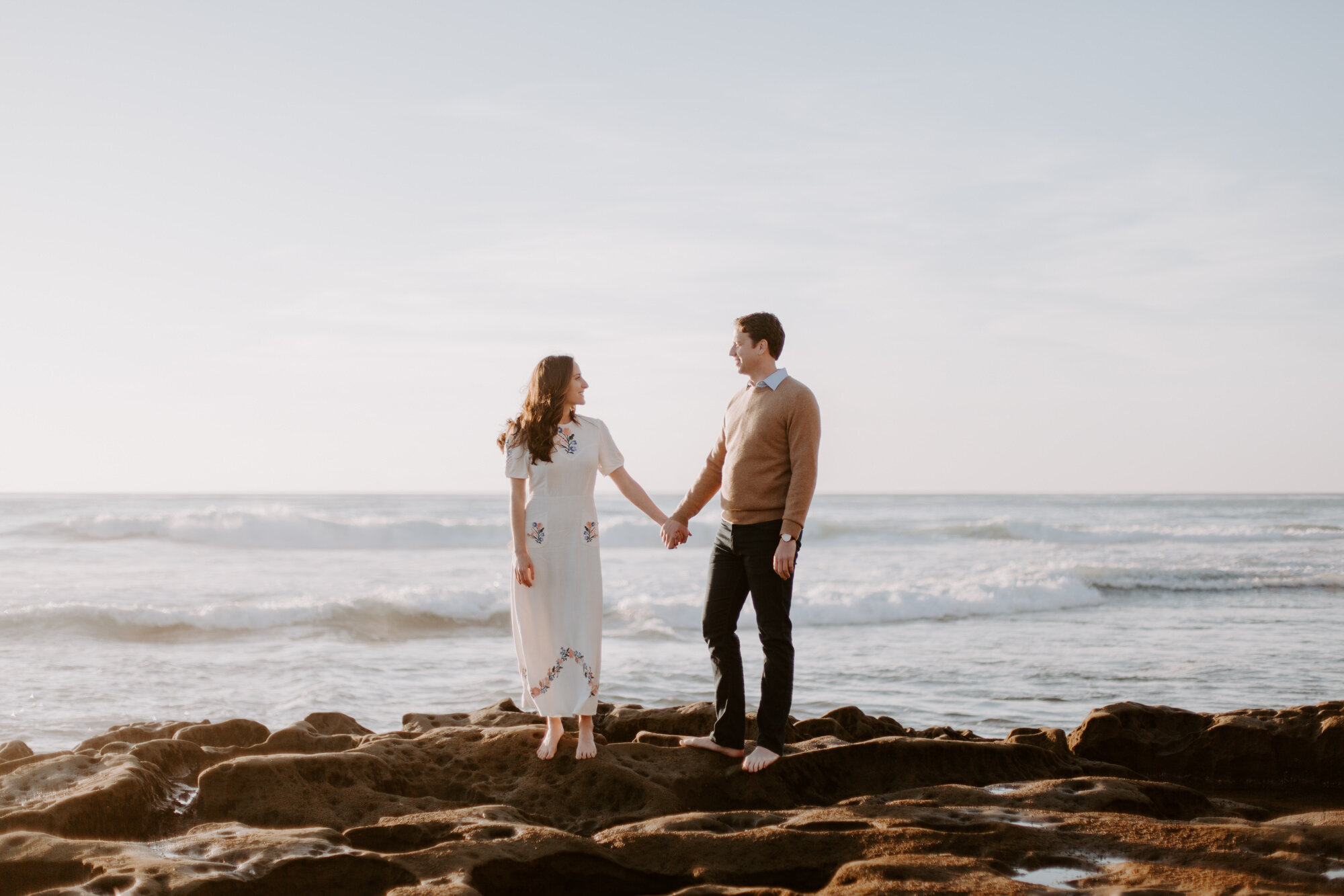 La Jolla Engagement Photos in San Diego with beach cliff and tide pools and on the sand.  Wore a white floral dress and took their engagement photos for their wedding by Kara Reynolds photography