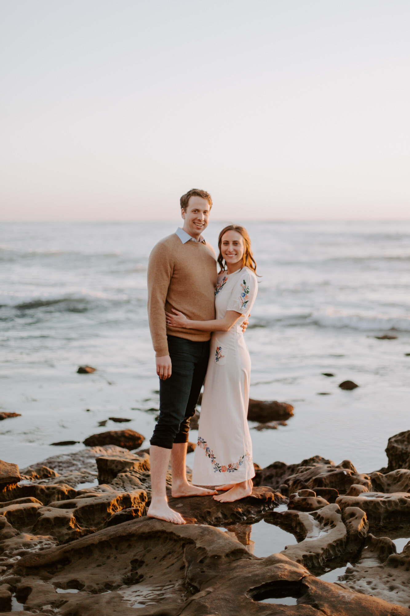 La Jolla Engagement Photos in San Diego with beach cliff and tide pools and on the sand.  Wore a white floral dress and took their engagement photos for their wedding by Kara Reynolds photography