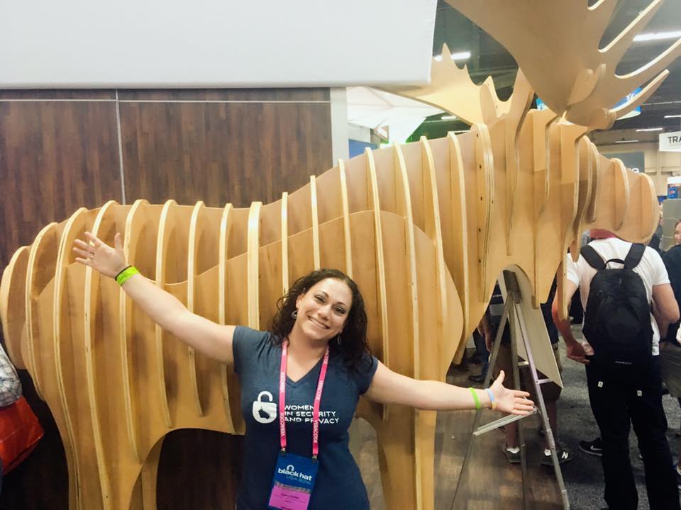 WISP Co-Founder, Debra J. Farber, on the Black Hat vendor floor, posing with Rapid7's moose.