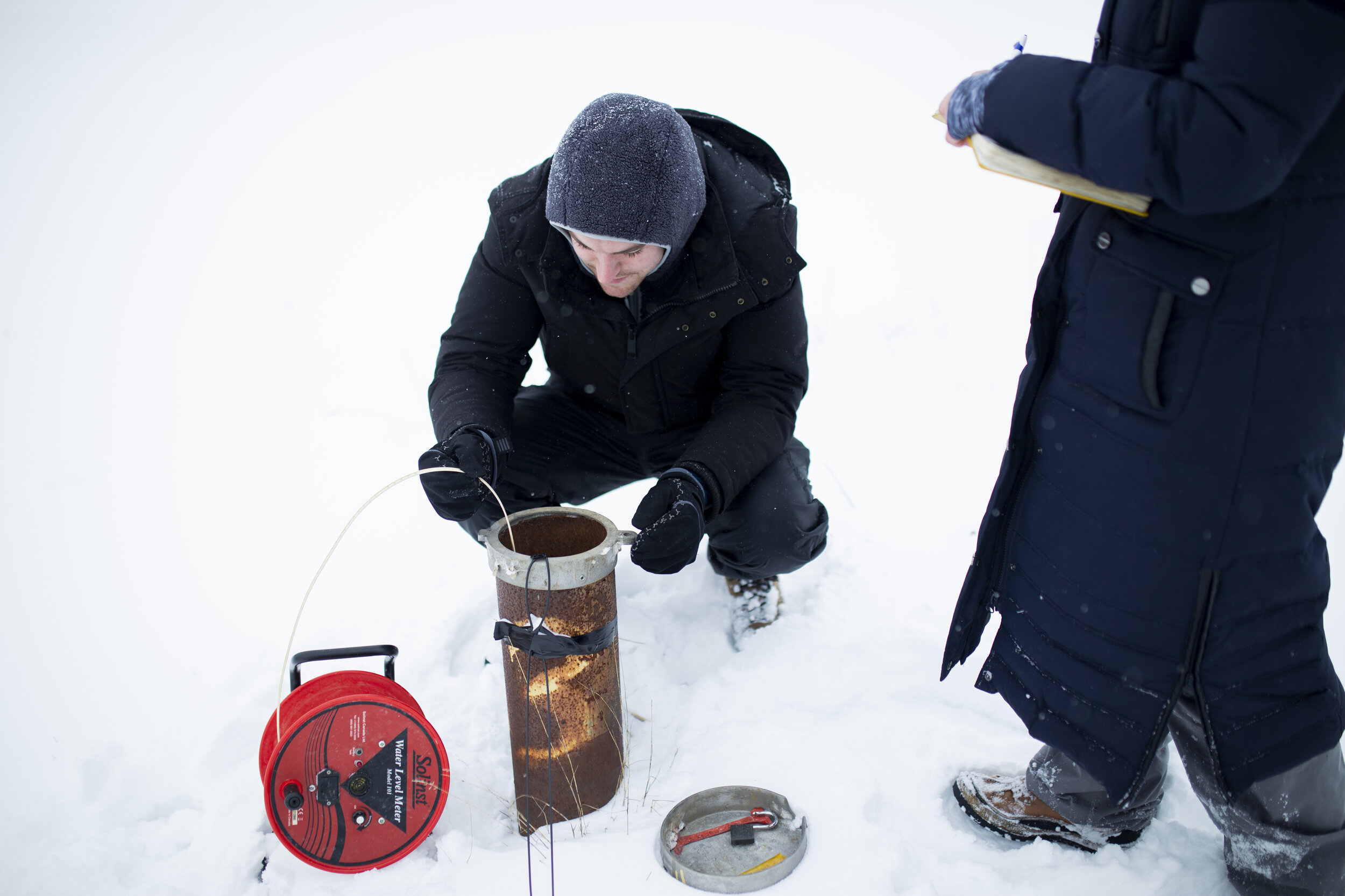  Wright instructs her assistant, Mitchell, as he uses a water level tape to measure the level of the groundwater well. 