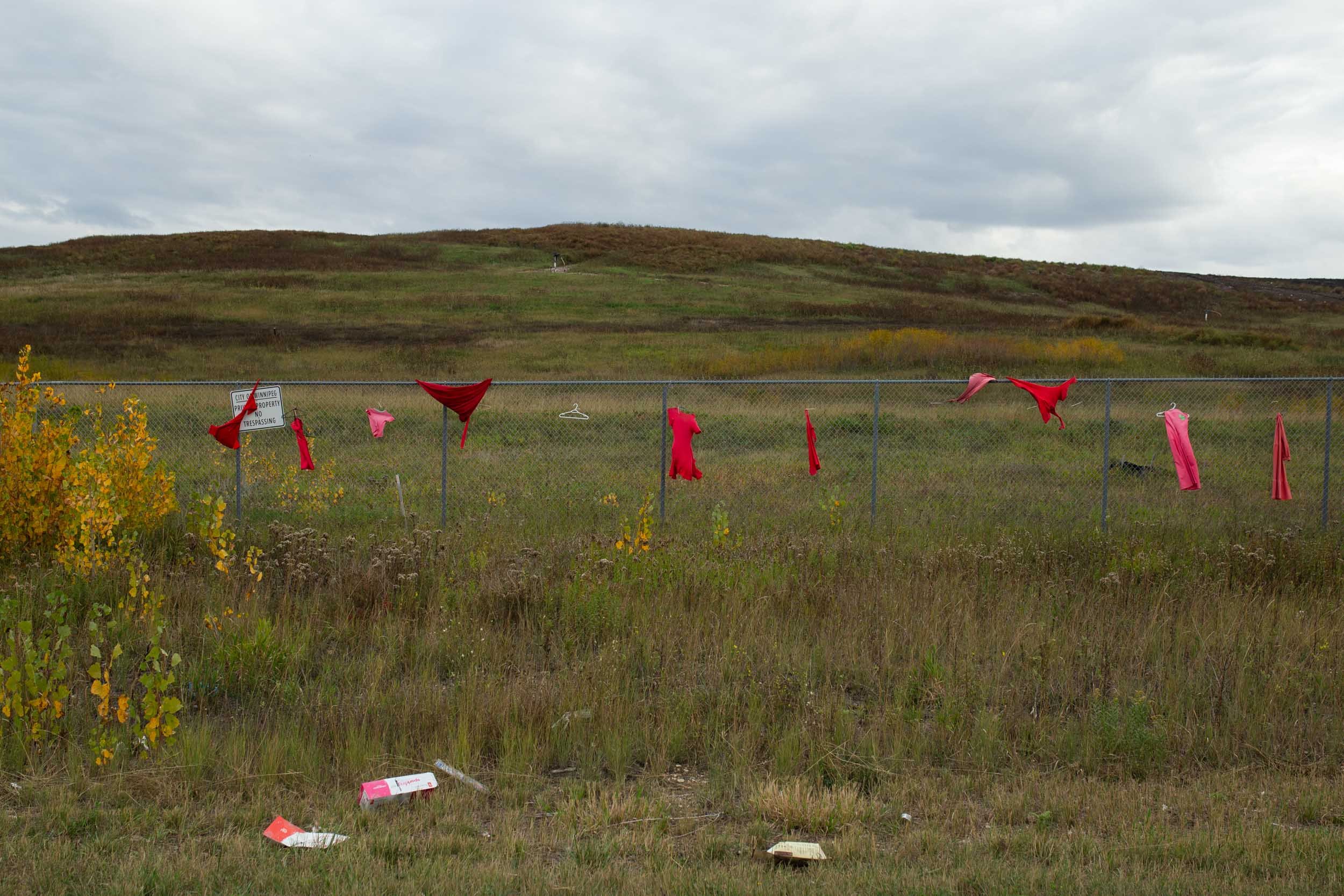  Up the road from Camp Morgan and in front of Brady Landfill, red dresses hang along the fence in memorial and advocacy for MMIWG2S. They were initially hung by the community as one of the earlier demonstrations and calls to action to  search the lan