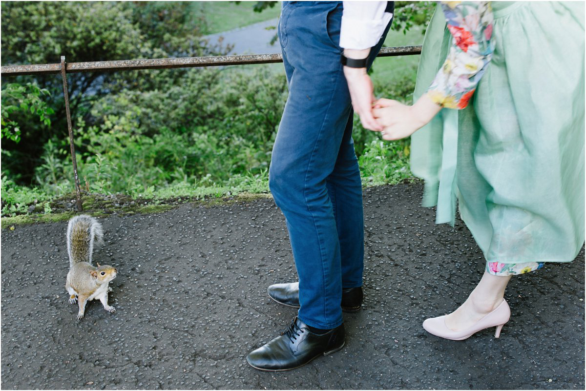  Bride in green dress and groom looking at a squirrel that came over to them in a park in Edinburgh  