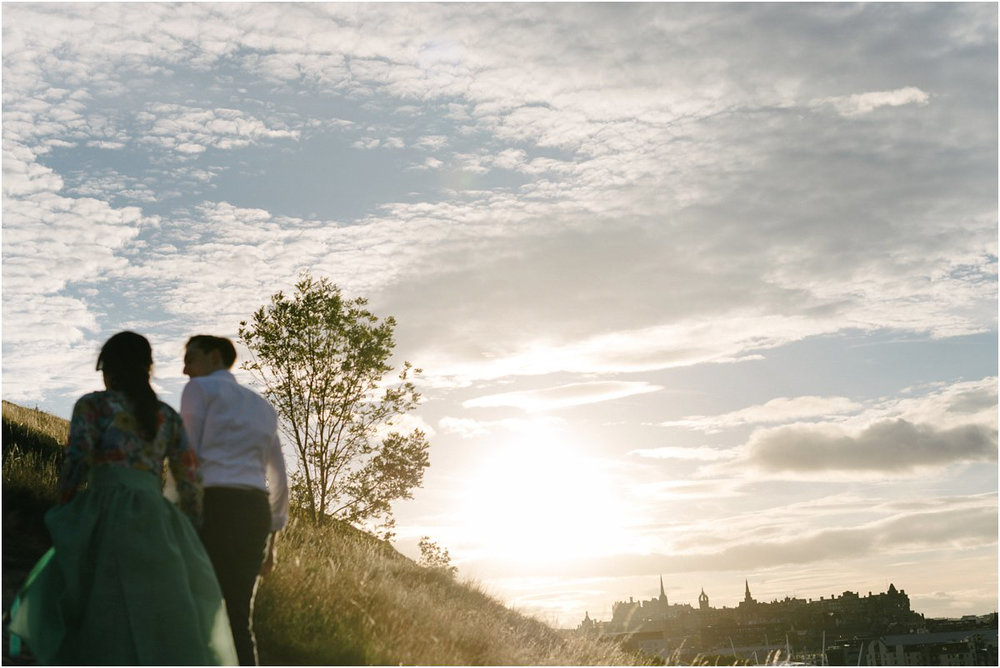  a young couple from the back walking up a hill in Edinburgh in a sunset 