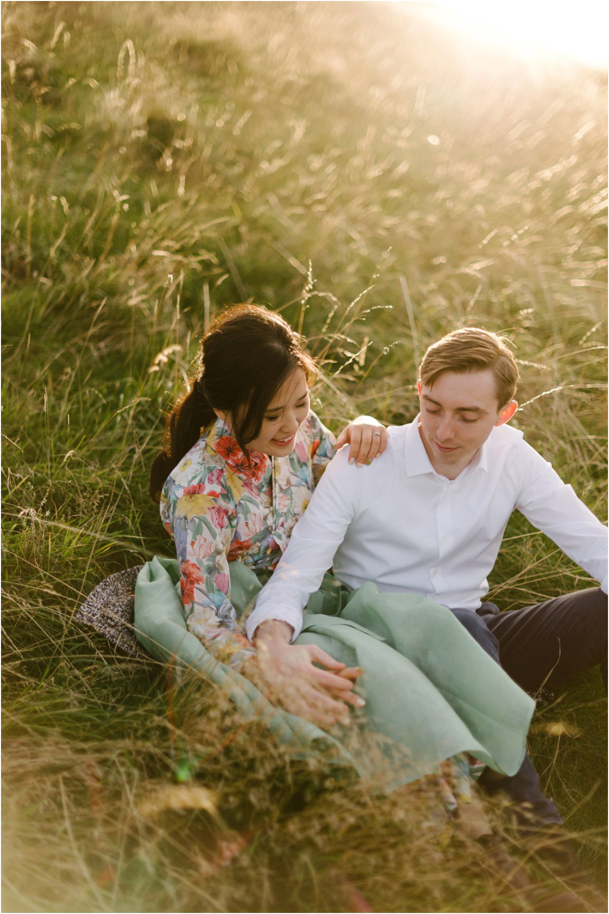  Korean girl and British boy sitting in tall grass holding hands in a sunset 