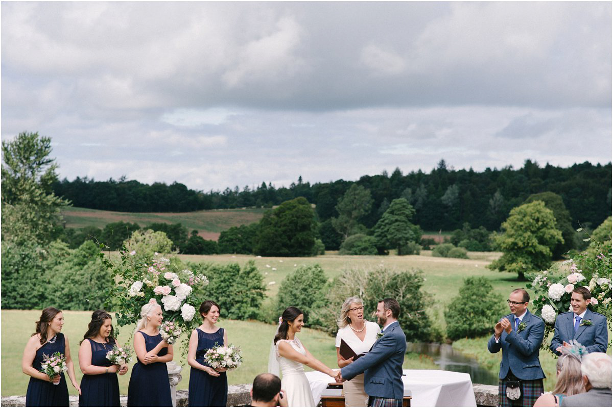  Summer Scottish castle wedding ceremony outdoors with bridesmaids in navy dresses and groomsmen in blue kilts in front of Blairquhan castle by Cro & Kow Photography 