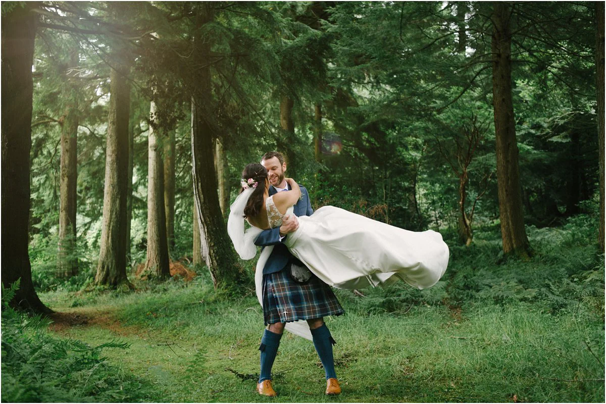 Groom lifts the bride in his arms in a forrest near Blairquhan castle in Scotland by Cro & Kow