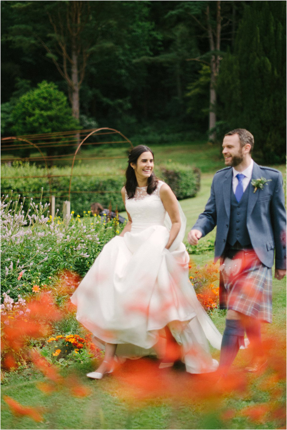  Newly married couple walking among red flowers in a garden of Blairquhan castle in Scotland by Cro & Kow 
