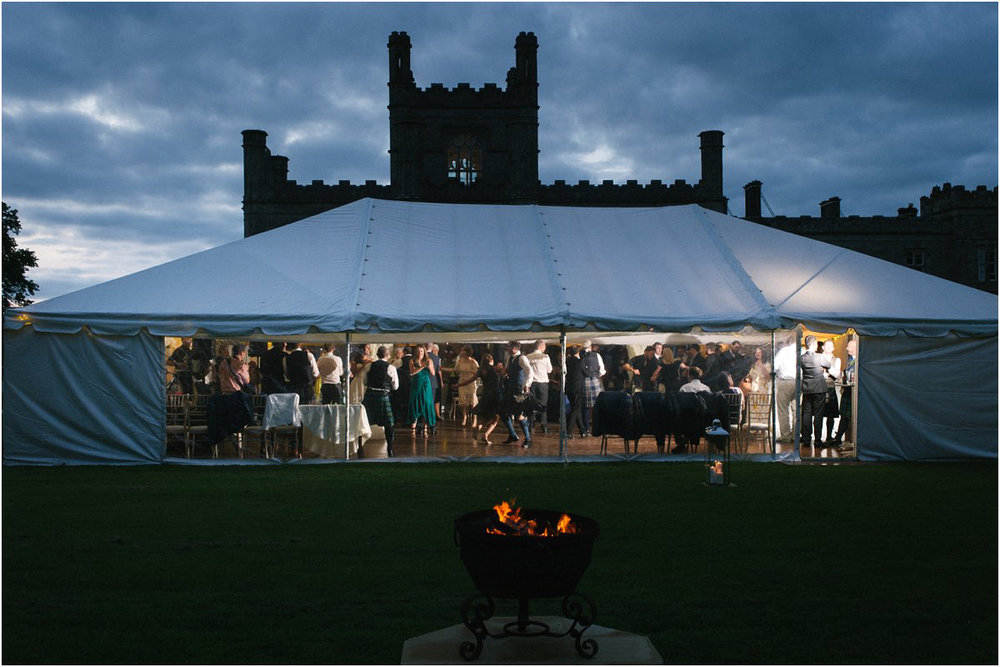  A lit marquee with translucent windows at dusk with a Scottish castle of Blairquhan during a summer wedding ceilidh dancing by Cro & Kow 