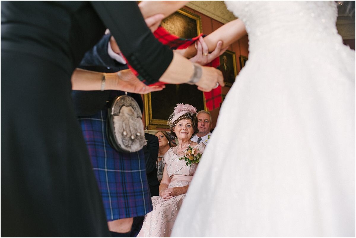  A couple tying a know with their tartan ribons in front of their friends and families at Winton castle wedding ceremony 
