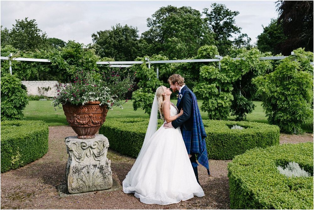  Married couple stealing a kiss during their portrait shoot at a walled garden at Winton castle Scotland  