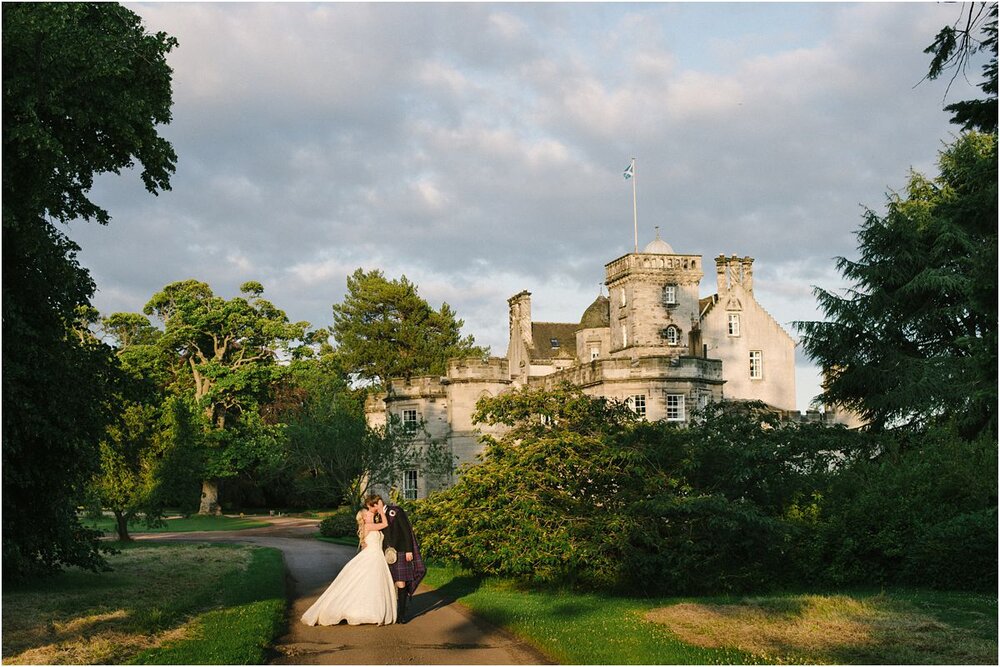  A young couple in front of their wedding venue at sunset during their Summer wedding at Winton castle Scotland  